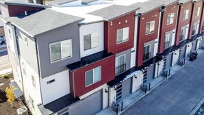A modern multi-story residential building with a mix of red and grey facades, balconies, and a clear driveway.
