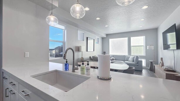 A modern kitchen with a large island, pendant lighting, and a view to the living area.