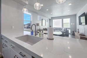 A modern kitchen with a large island, pendant lighting, and a view to the living area.