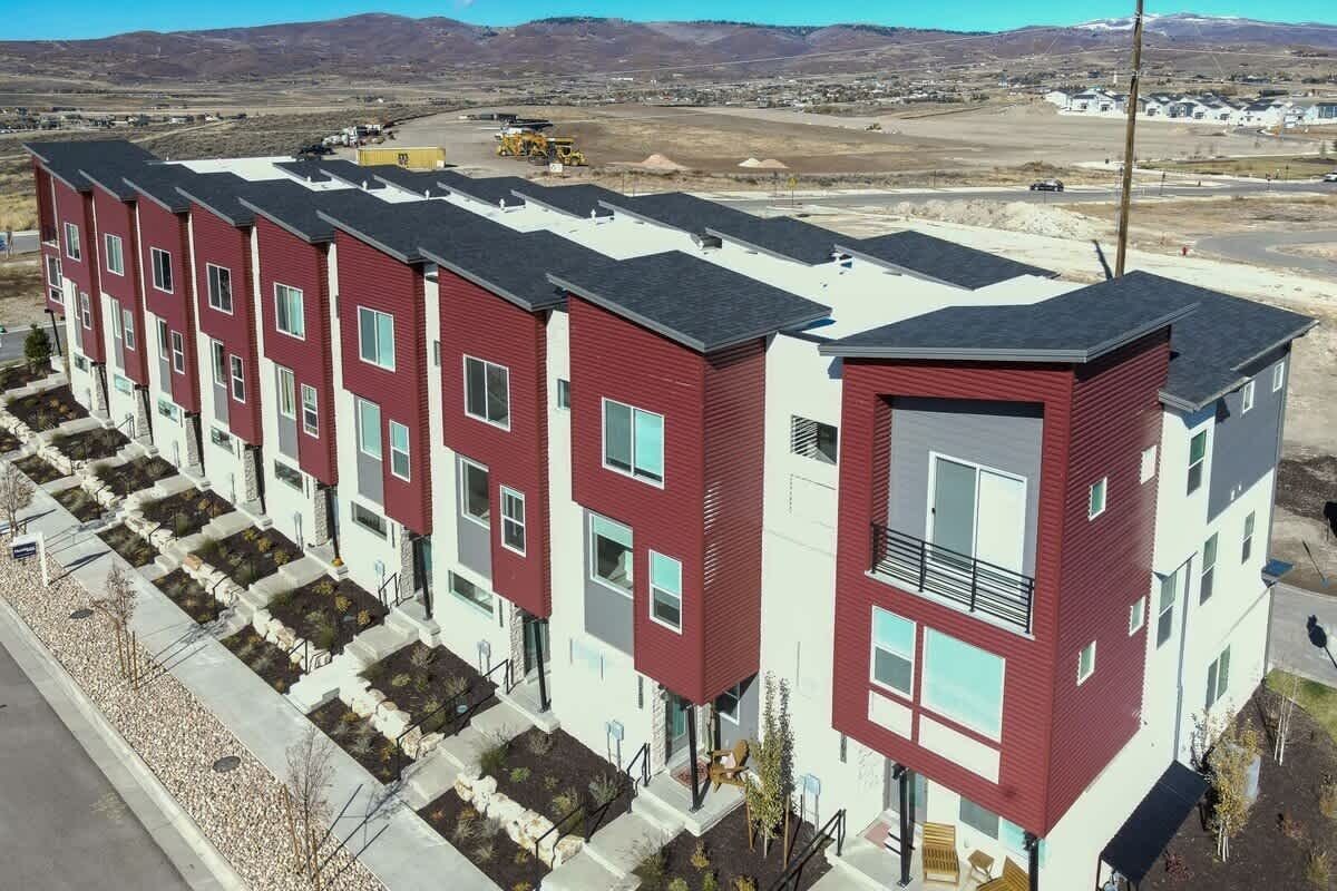 Un immeuble résidentiel à plusieurs étages, avec une façade rouge et blanche, un balcon au deuxième étage et un parking en arrière-plan.