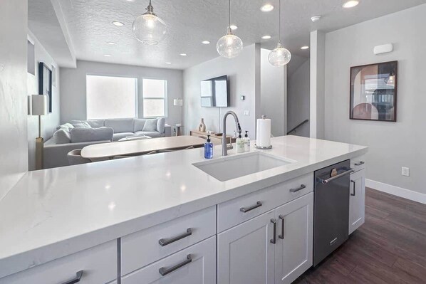 A modern kitchen with a large island, built-in dishwasher, and pendant lighting.