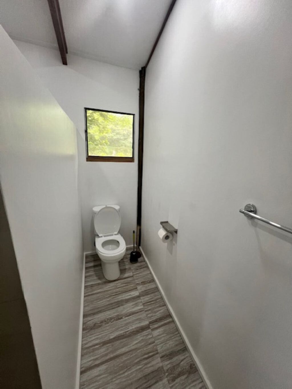 A narrow, modern bathroom with a toilet, a window, and a shower area.