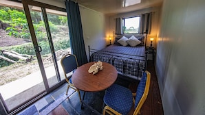 Ein kleiner, gemütlicher Raum mit einem Bett, einem Tisch und Stühlen. Ein Fenster bietet Blick auf grüne Natur.