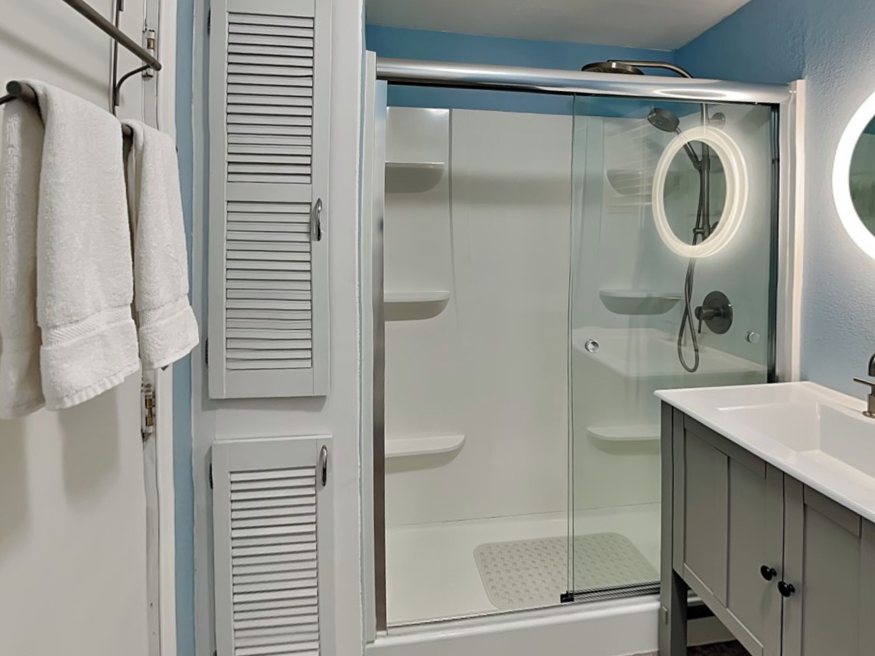 A modern bathroom with a glass-enclosed shower, a white sink, and a vanity cabinet.