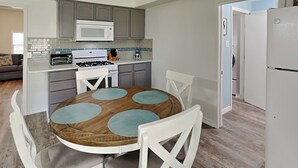 A modern kitchen with a round wooden table, white chairs, a microwave, a stove, and a refrigerator. - The Charming Cozy Cottage by Miss Kitty’s (Rockport)