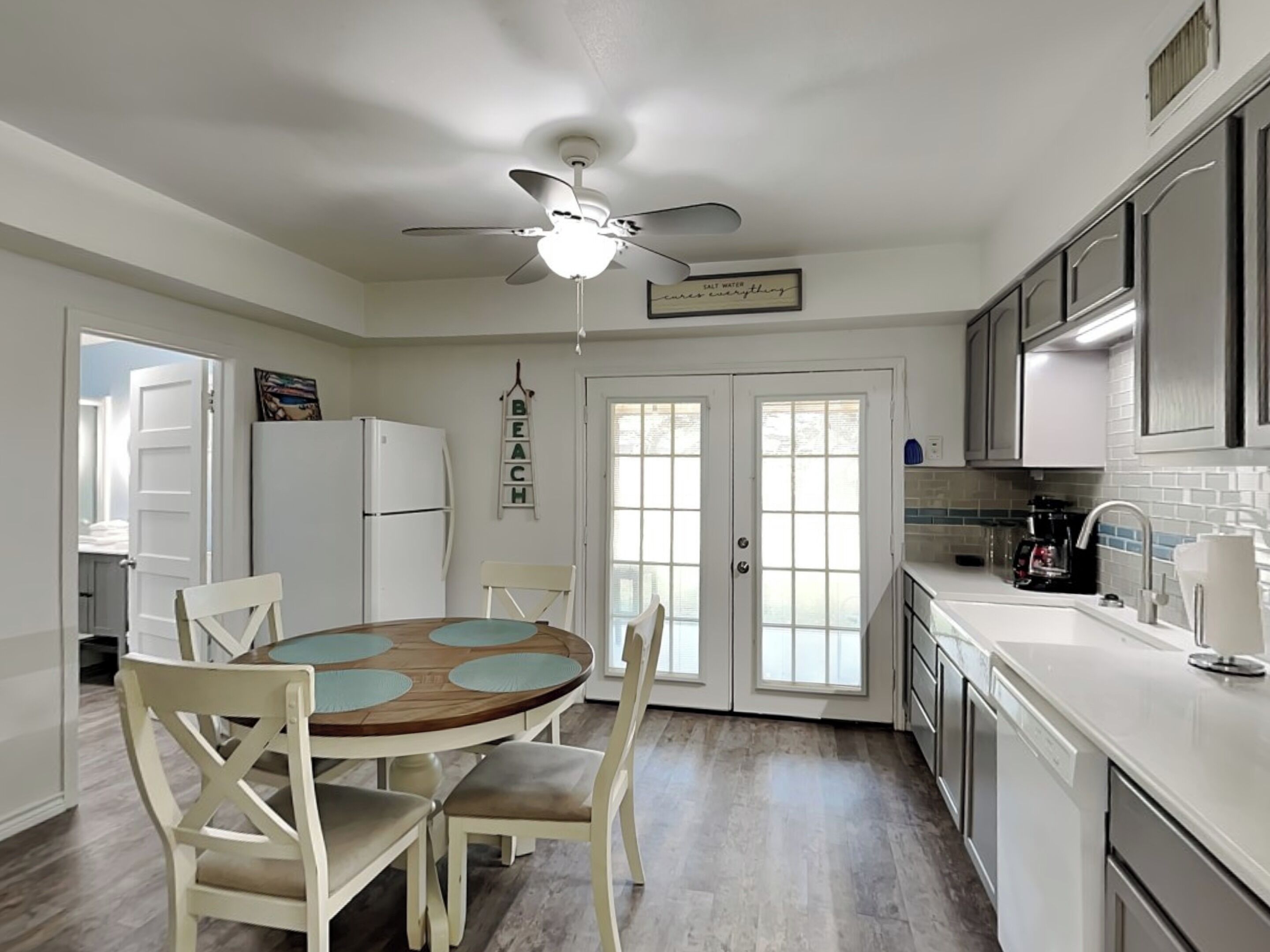 A kitchen with a dining table, chairs, a ceiling fan, a refrigerator, and a coffee maker.