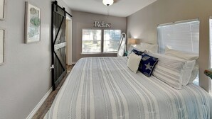 A bedroom with a large bed, a wardrobe, a ceiling fan, and a window with blinds. - The Charming Cozy Cottage by Miss Kitty’s (Rockport)