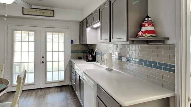 A kitchen with white cabinets, a white countertop, and a backsplash with blue and white tiles. There is a coffee maker on the counter and a small lighthouse decoration on the shelf. - The Charming Cozy Cottage by Miss Kitty’s (Rockport)