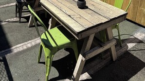 A wooden table and chairs set outdoors with a wooden fence and string lights in the background. - The Bat & Ball Hostel (Redfern)