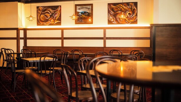 A restaurant interior with booths and tables, wooden paneling, and artwork on the walls. - The Bat & Ball Hostel (Redfern)