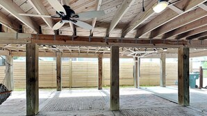 Una struttura aperta in legno con una ventola a soffitto, pavimento in mattoni e un recinto di legno sullo sfondo.