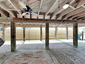 An open wooden structure with a ceiling fan, brick flooring, and a wooden fence in the background. - Treehouse Haven by Ryson Vacation Rentals (Galveston)