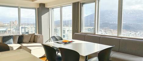 A modern interior with a large table and chairs, a sofa, and large windows offering a city view.