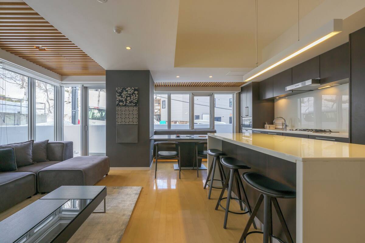 A modern kitchen with a central island, bar stools, and a dining area with a sofa and chairs.