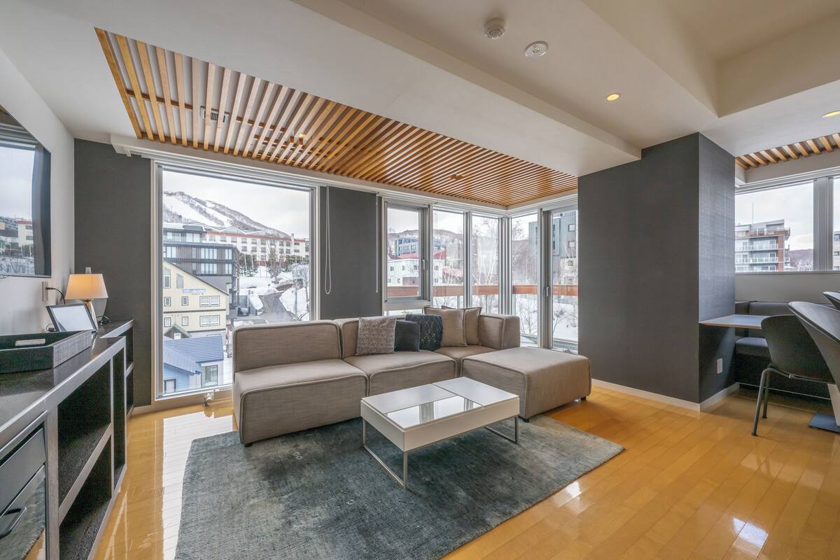 A modern living room with a sectional sofa, a glass coffee table, and a desk area.