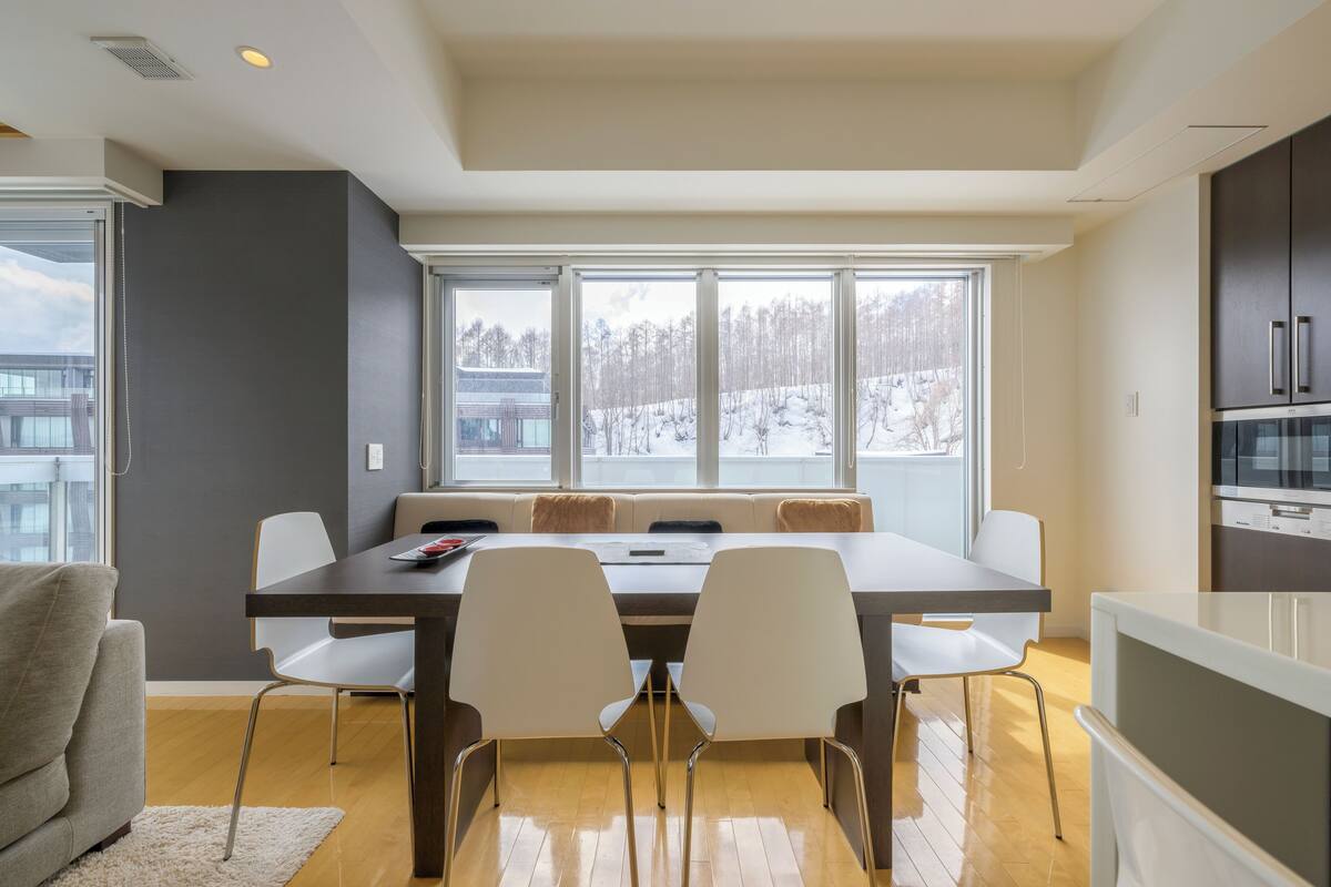 A modern kitchen with a dining area, large windows, and a view of a snowy landscape.