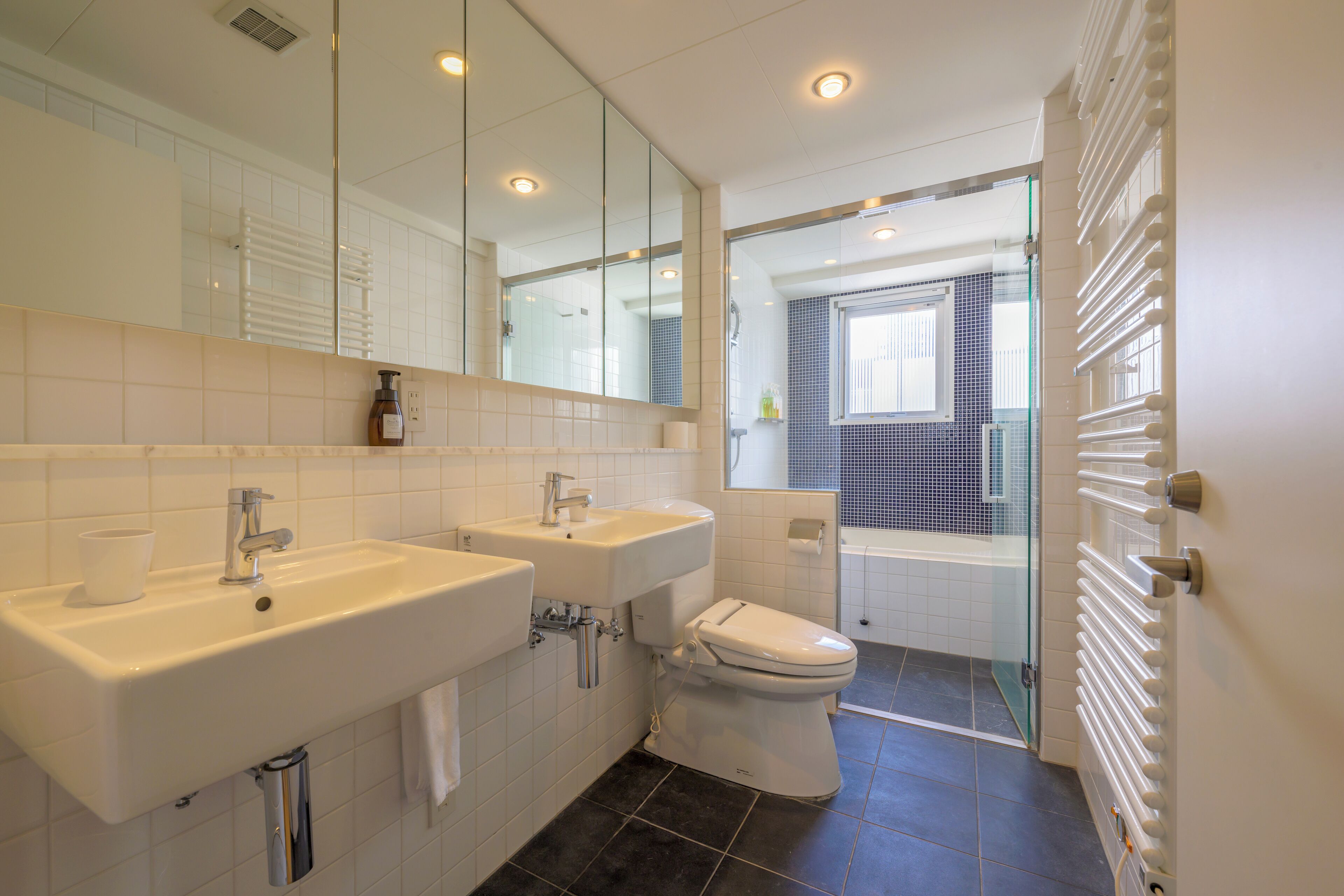 A modern bathroom with two sinks, a toilet, and a glass shower enclosure.