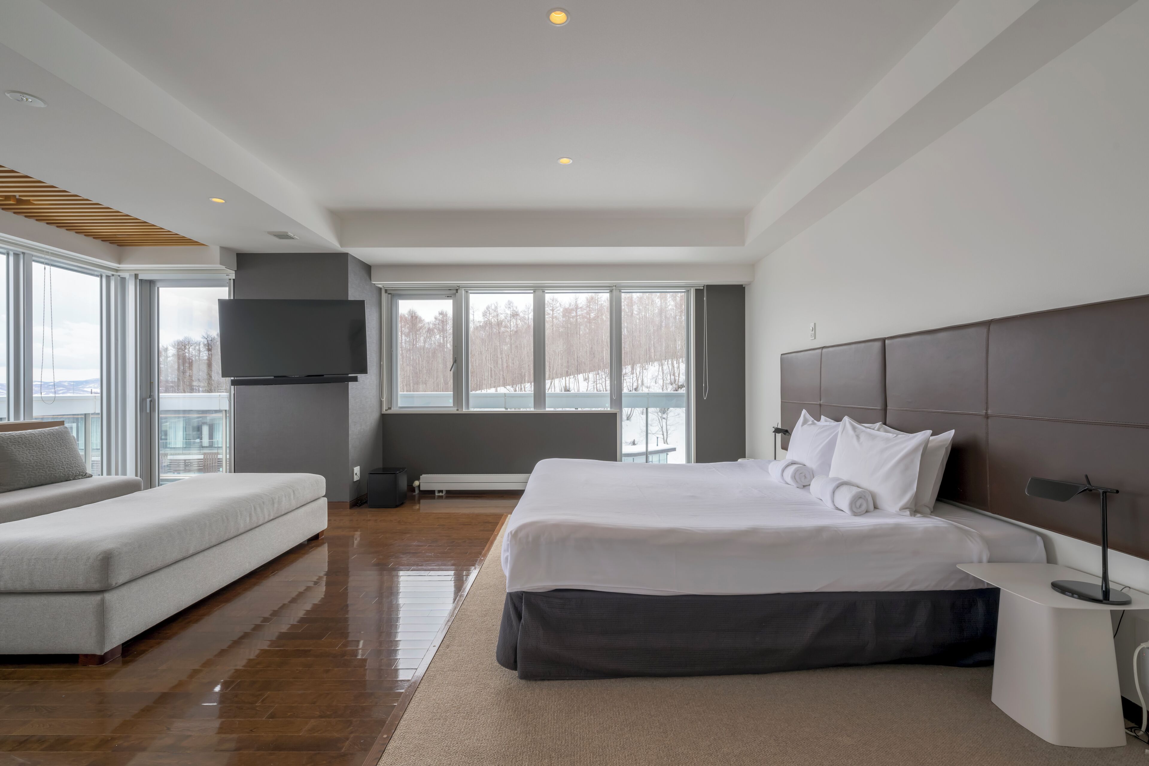 A modern hotel room with a large bed, a sofa, a flat-screen TV, and a view of the outdoors.
