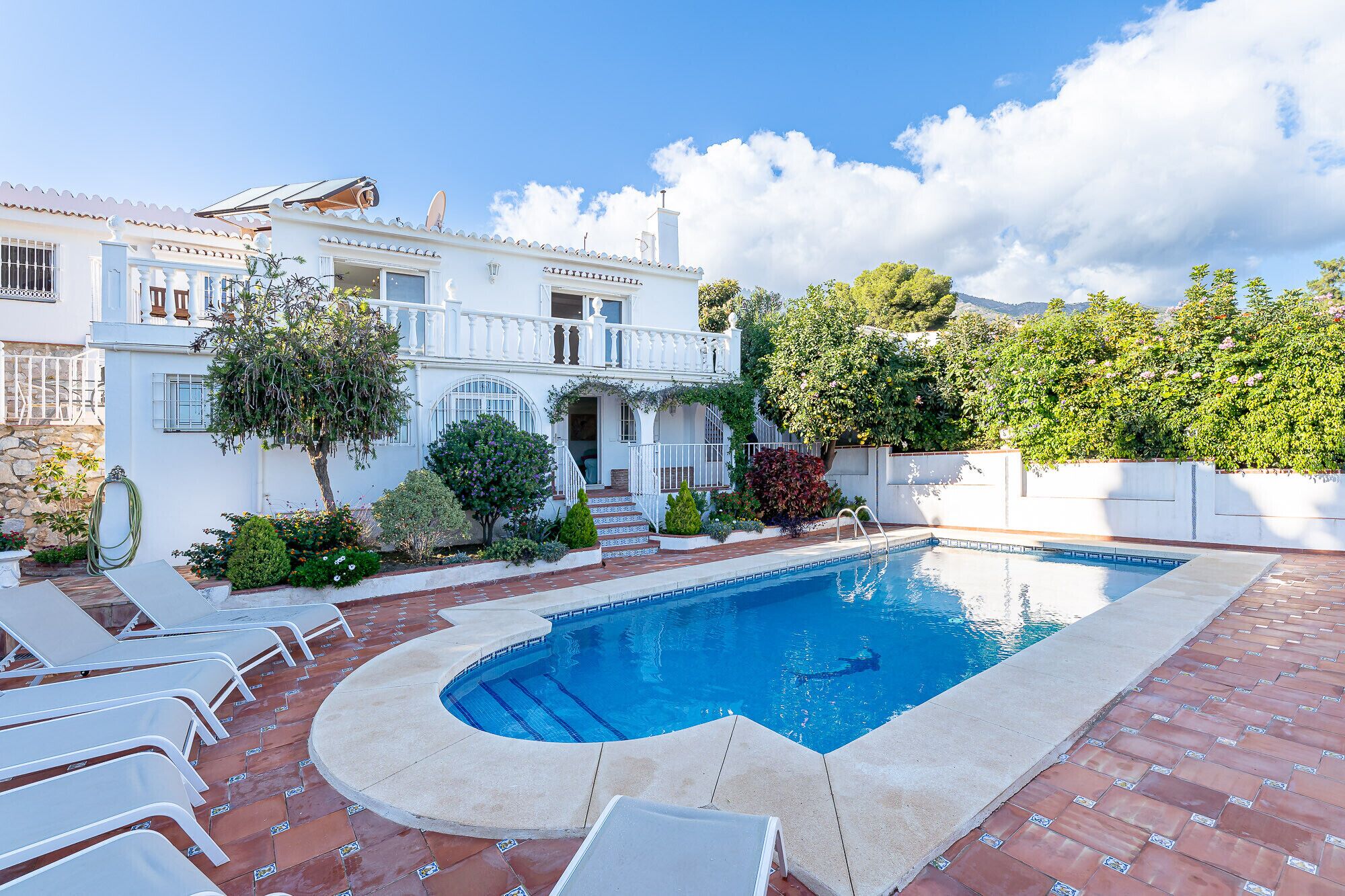 Eine weiße Villa mit Swimmingpool, einer überdachten Terrasse und einem Garten mit verschiedenen Pflanzen.