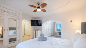 Une chambre avec un grand lit, un ventilateur de plafond, une télévision et une vue sur l’extérieur.