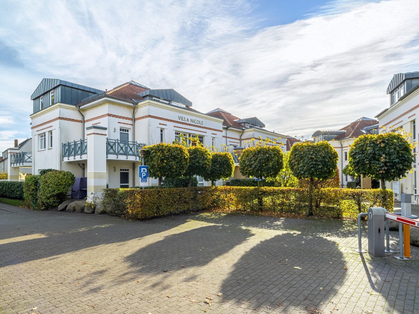 Una villa llamada "Villa Nicole" con un patio empavedado, una entrada con portón y un letrero de estacionamiento.