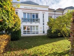 Un bâtiment à deux étages appelé « Villa Nicole », doté d’un balcon, de grandes fenêtres et d’une pelouse bien entretenue.
