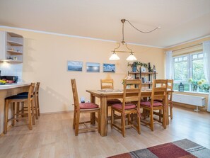 Un comedor con una mesa y sillas de madera, una lámpara colgante y una ventana con vistas a zonas verdes.