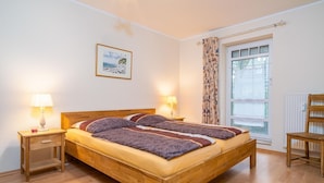 Une chambre à coucher avec un lit en bois, deux tables de chevet avec des lampes, une fenêtre avec des rideaux et un tableau encadré au mur.
