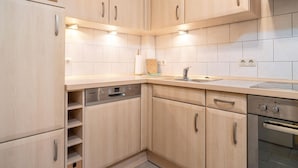 Une cuisine moderne avec des meubles en bois clair, un lave-vaisselle encastré, un four en acier inoxydable et un pare-feu en carrelage.