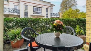 Une terrasse avec une table ronde et des chaises, un pot de fleurs et un bâtiment en arrière-plan.