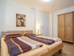 A double bed with patterned bedding, a wooden headboard, a wall-mounted giraffe painting, a bedside lamp, and a wooden wardrobe. - Villa Sonja - Apartment 08 - Comfortable vacation apartment with covered terrace in the (Zingst (Ostseeheilbad))