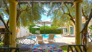 A covered outdoor area with a pool, lounge chairs, and umbrellas.