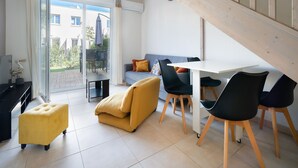 A modern living room with a sofa, ottoman, dining table, chairs, and a staircase. - Bright villa 6 ppl, garden, close to the sea (Sérignan)