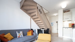 A modern living room with a grey sofa, yellow cushions, a black coffee table, and a wooden staircase leading to a kitchen area. - Bright villa 6 ppl, garden, close to the sea (Sérignan)