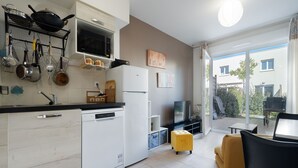 A modern kitchen with a dishwasher, microwave, and various utensils. There's a dining area with a yellow ottoman and a TV. - Bright villa 6 ppl, garden, close to the sea (Sérignan)
