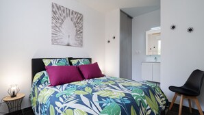 A bedroom with a bed, a chair, a small table, a mirror, and a ceiling fan.