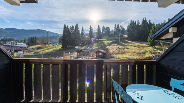 Un balcon offrant une vue sur un paysage montagneux, une petite construction en bois et une table avec des chaises.
