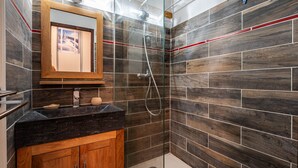 Une salle de bain avec un meuble-lavabo en bois, un miroir et une douche dotée d’une porte en verre.