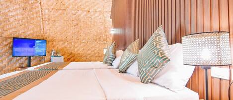 A hotel room with a large bed, a TV on a stand, a lamp, and a woven wall design.