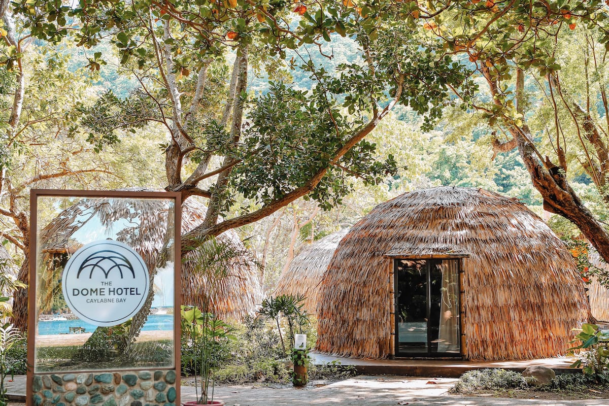 A thatched-roof structure with a sign for The Dome Hotel Caylanbe Bay.