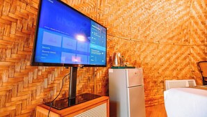 Una habitación con televisión montada en una pared de madera, un refrigerador y una cama.