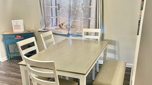 A dining area with a table, four chairs, a bench, and a window with a view of the sea. - Charming 3-bedroom house with comfortable beds close to the beach! (Long Beach)