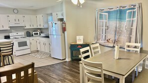 A kitchen with white cabinets, a refrigerator, a stove, and a microwave. There is a dining table with chairs and a ceiling fan. - Charming 3-bedroom house with comfortable beds close to the beach! (Long Beach)