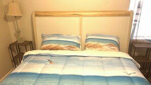 A bed with a beach-themed duvet, a bedside lamp, and a small wooden nightstand. - Charming 3-bedroom house with comfortable beds close to the beach! (Long Beach)