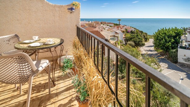 A balcony with a table and chairs, overlooking a coastal town and the sea. - Cozy home in Nerja with WiFi (Nerja)