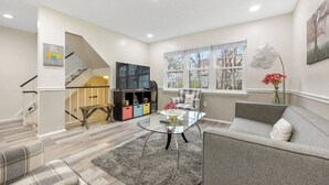 Una sala de estar moderna con una escalera, una mesa de centro de vidrio, un sofá gris y una estantería.