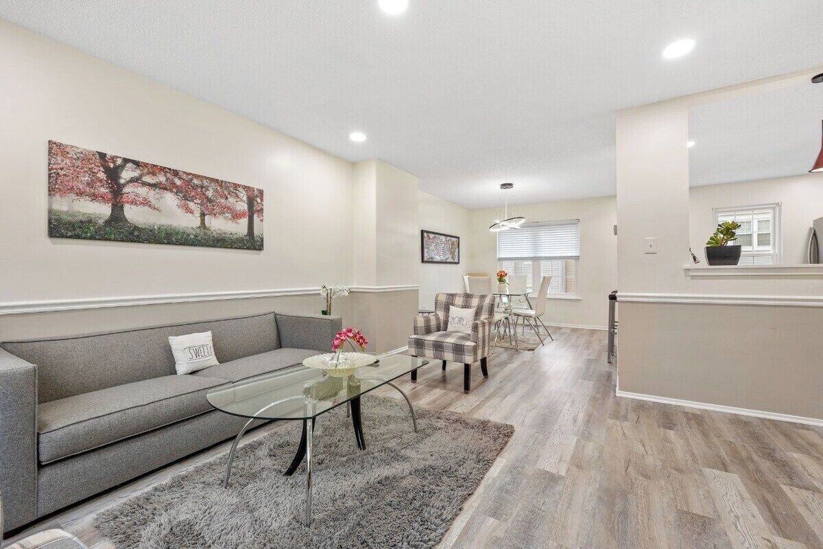 A modern living room with a grey sofa, a glass coffee table, and a dining area with a white table and chairs.