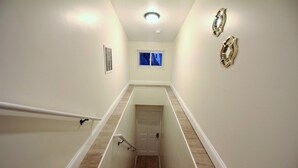 Una escalera estrecha con barandilla, una puerta al final e una ventana con vistas a edificios.