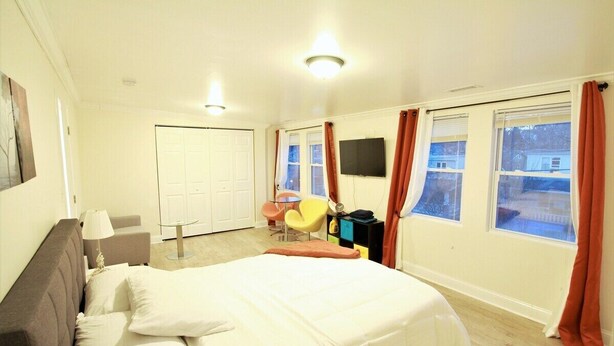 Un dormitorio con cama, escritorio, silla, televisor y ventanas con cortinas.