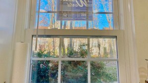 A window with a view of trees and a building in the background. - Efficiency Bright BSMNT APT- DC 20m IAD-10m Metro (Reston)